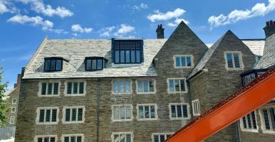 An old-fashioned stone college building with slate tiled roof, and a crane arm extending across the view